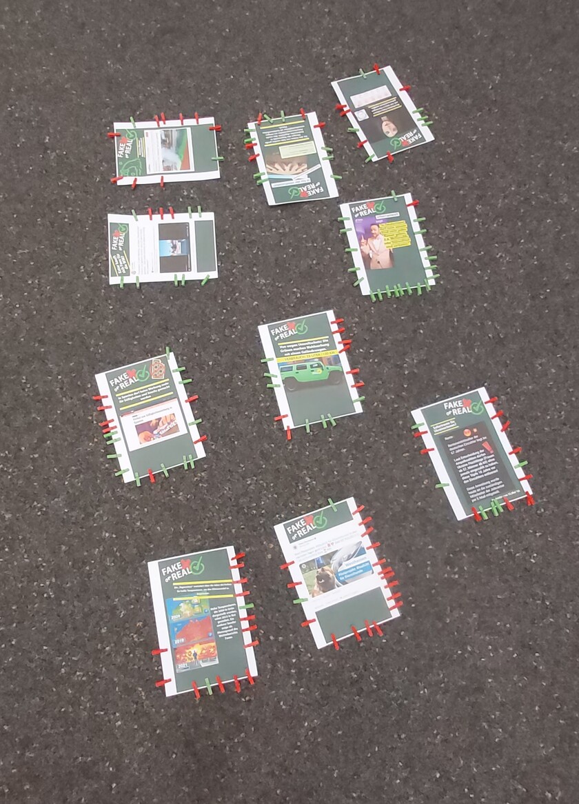 Mehrer Zettel mit einzelnen Nachrichten liegen auf dem Boden. An ihnen hängen mehrere rote und grüne Wäscheklammern.