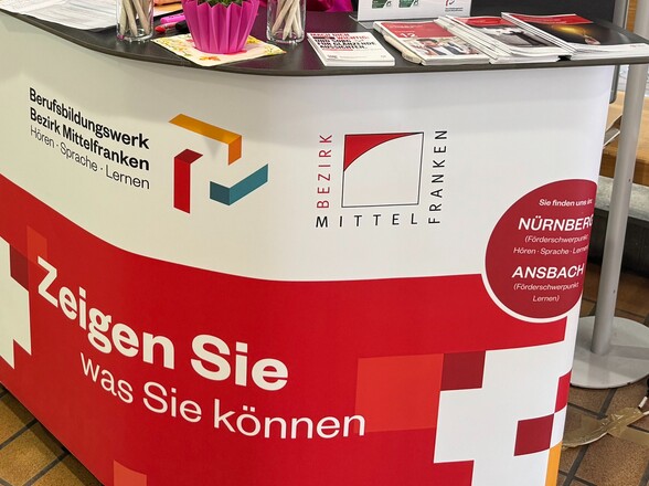 Ein Stand-Tisch des BBWs. Darauf zu sehen ist unter anderem das Logo des BBWs Nürnberg und der Satz "Zeig was du kannst".